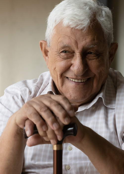 Happy elder 80s man with disability holding knob of cane
